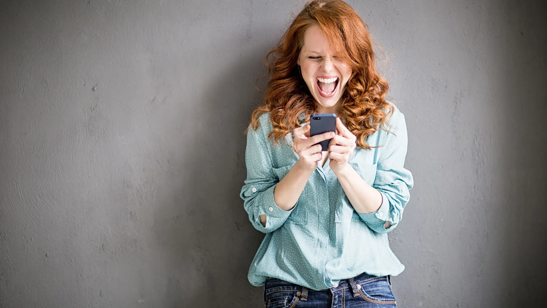 Eine junge Frau jubelt begeistert über ihr Smartphone